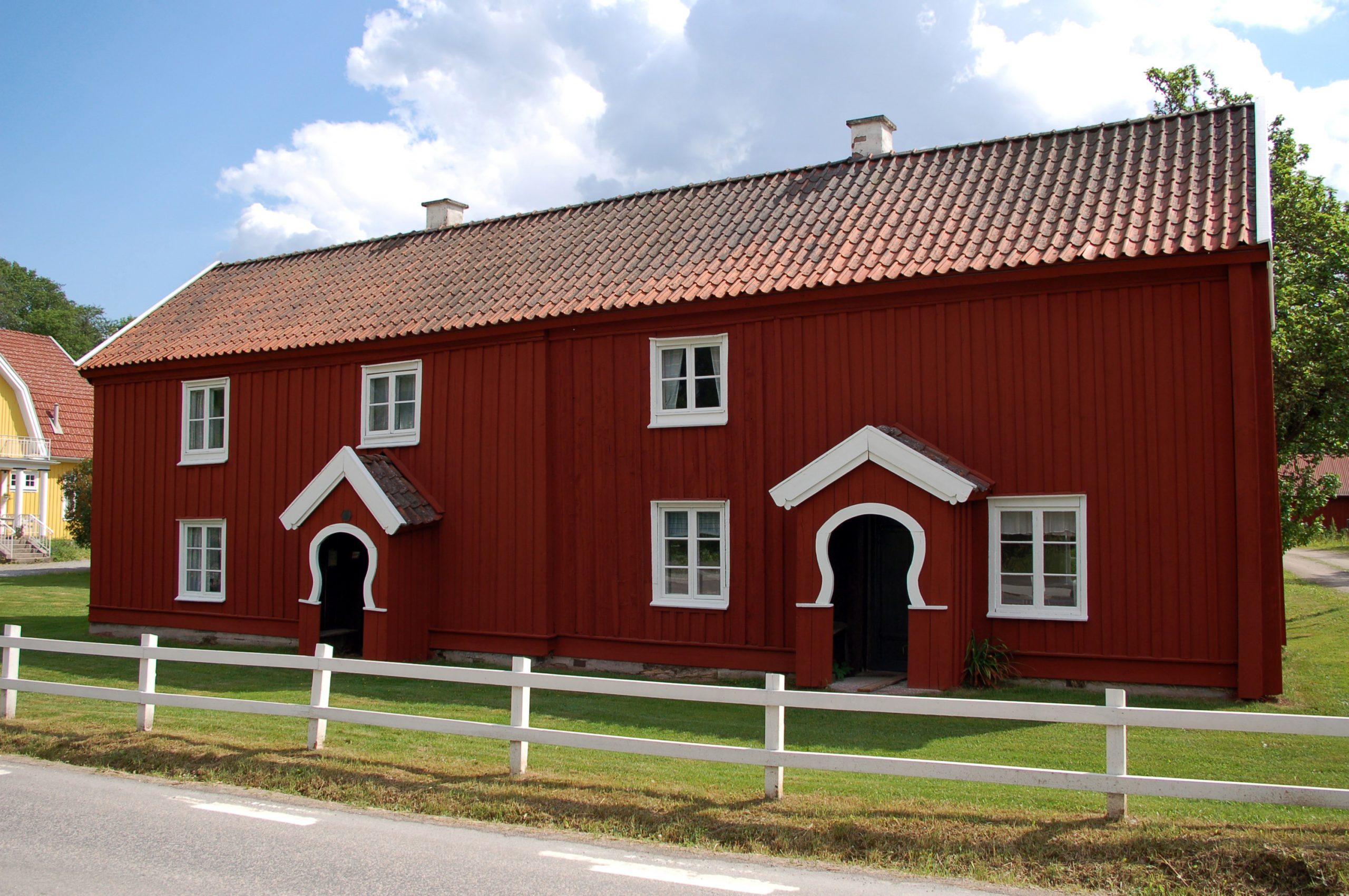 Bild på Bäckagården i Marbäck, en röd träbyggnad i två våningar med vita fönster.