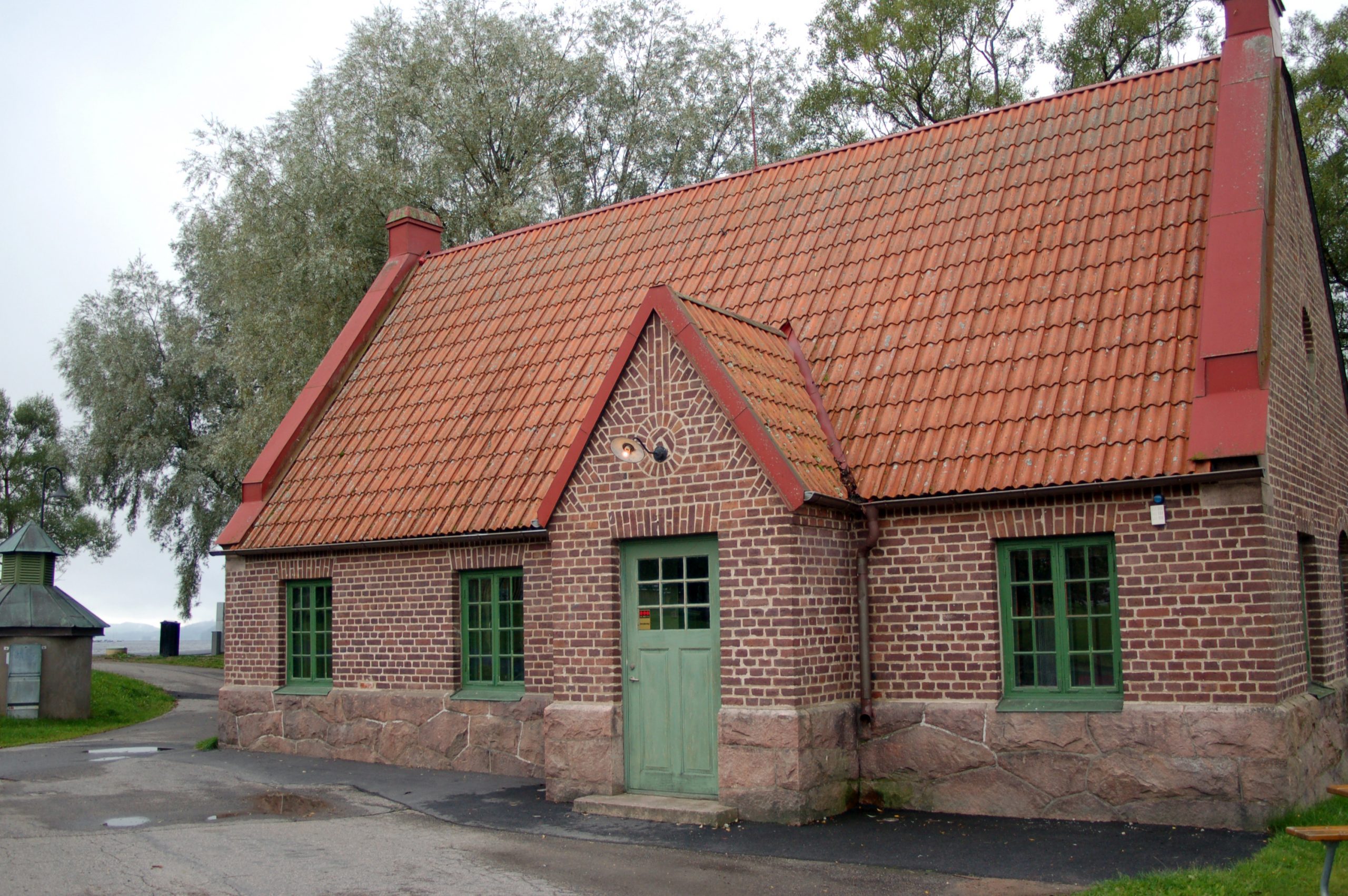 Bild på Gamla vattenverket i Ulricehamn. En låg röd tegelbyggnad me grön dörr och gröna fönster.