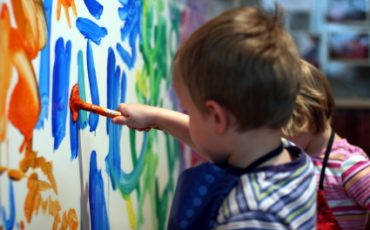 Bild på en tre-åring som målar på en vägg med blått och orange
