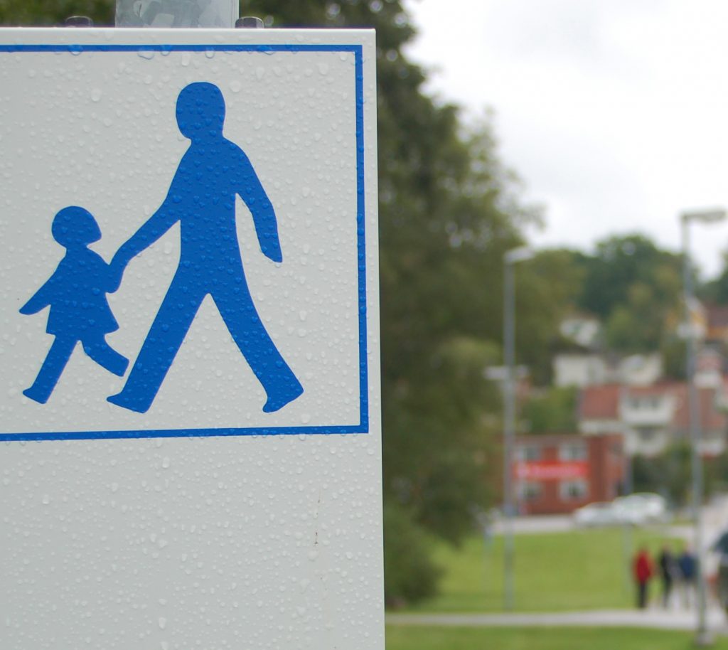 Bild på en vit skylt med två blå gubbar som symboliserar promenadstråk att följa.