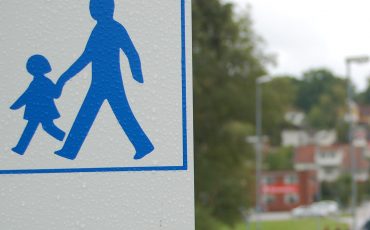 Bild på en vit skylt med två blå gubbar som symboliserar promenadstråk att följa.