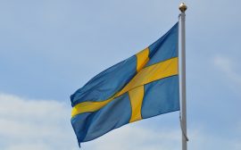 Svenska flaggan. Blå med ett gult kors, vajar på en flaggstång