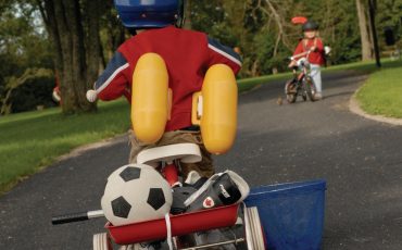 Bild på barn på trehjuling med fotboll på flaket och simpuffar på ryggen.