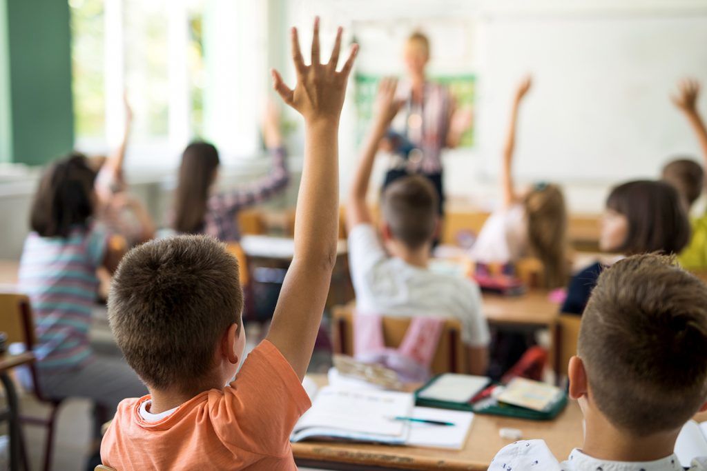Bild på barn som räcker upp handen i ett klassrum