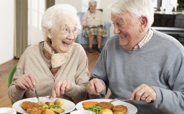 Två äldre personer som äter mat och ser glada ut