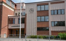 Bild på en skolentré med en klocka. Ovanför dörren står Stenbocksskolan.