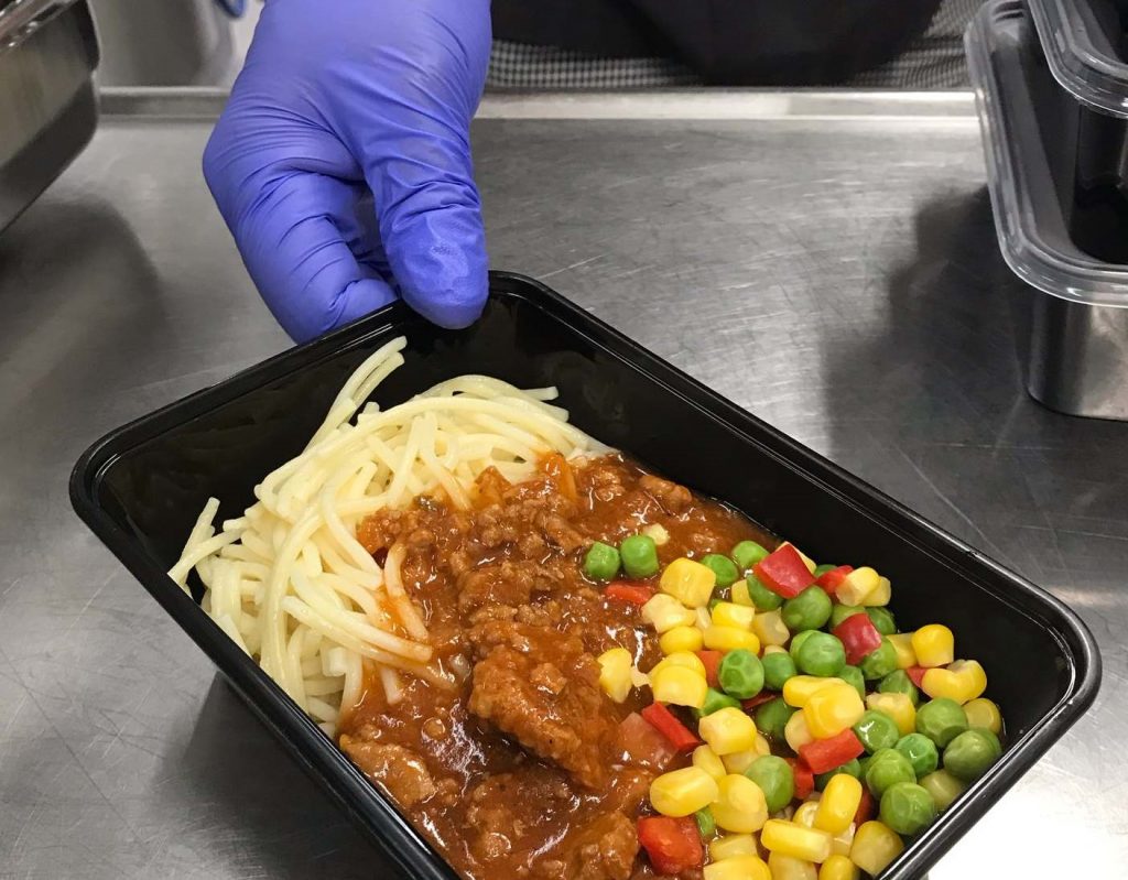 En hand som håller fram en lunchlåda innehållande spagetti med köttfärssås och grönsaker