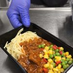 En hand som håller fram en lunchlåda innehållande spagetti med köttfärssås och grönsaker