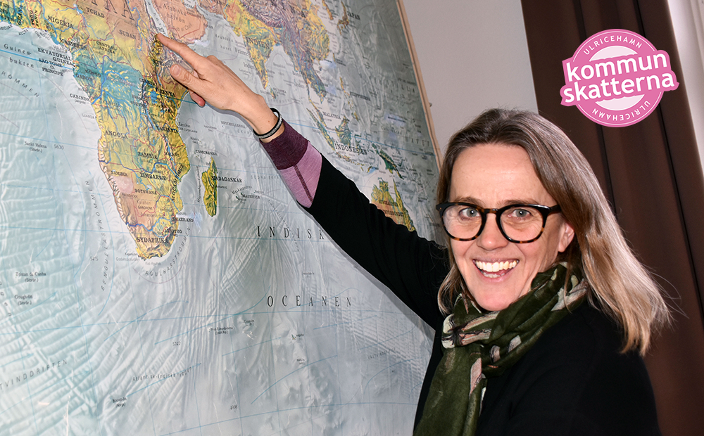 Karin har glasögon och pekar ut Eritrea på en stor världskarta som sitter på väggen.