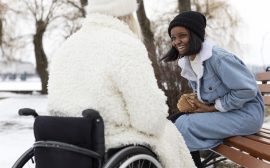 Skrattande kvinna på bänk mittemot en kvinna i rullstol