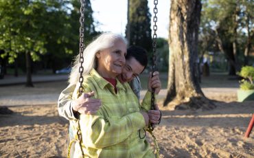 En äldre kvinna sitter på en gunga. Ett barn kramar henne