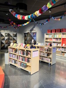 Ungdomsavdelningen, här står flera bokhyllor med massor av färgglada böcker. I taket hänger en girland av garnbollar i alla möjliga fätger.