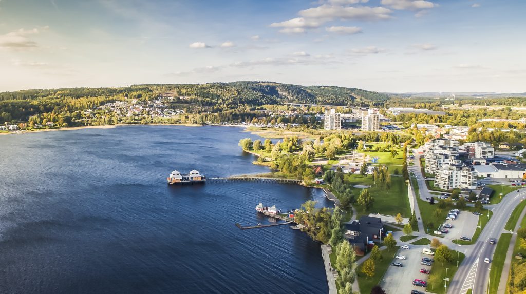 Flygfoto över Ulricehamns centrum, där kallbadhuset syns i sjön, berg i bakgrunden och delar av stadskärnan.