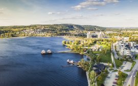 Flygfoto över Ulricehamns centrum, där kallbadhuset syns i sjön, berg i bakgrunden och delar av stadskärnan.