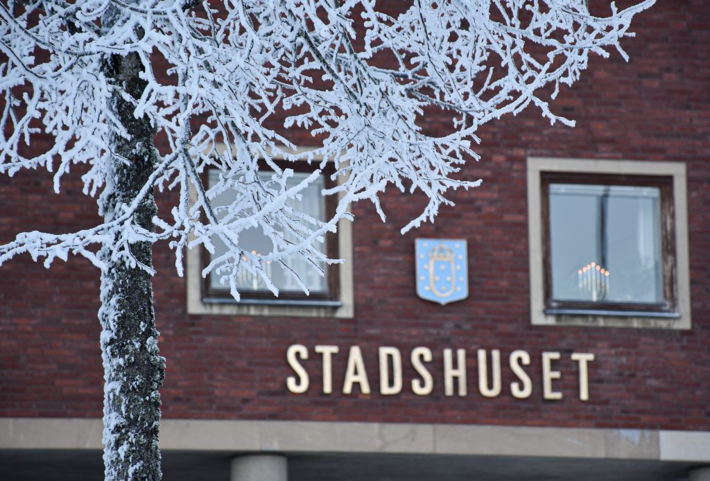 En röd tegelbyggnad med texten stadshuset på väggen. Framför byggnaden, ett träd med frost i grenarna.