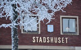 En röd tegelbyggnad med texten stadshuset på väggen. Framför byggnaden, ett träd med frost i grenarna.